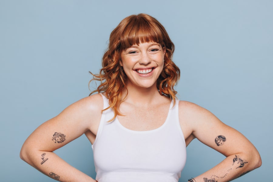Happy woman in a white tank top with tattoos on her arms